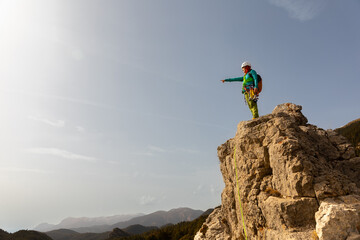 A person is standing on a rocky mountain top, pointing to the sky. Concept of adventure and...