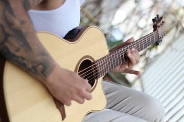 Melodic Reverie: Young Tattooed Musician Playing Acoustic Guitar on Balcony