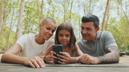 Happy family, mom dad and daughter, spending time together, family using smart phone looking at...
