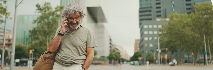 Friendly middle aged man with gray hair and beard wearing casual clothes using his mobile phone,...
