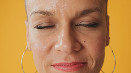 Close up portrait of young hairless woman stands with her eyes closed, isolated on yellow background in studio