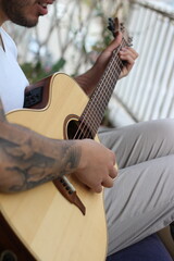 Melodic Reverie: Young Tattooed Musician Playing Acoustic Guitar on Balcony