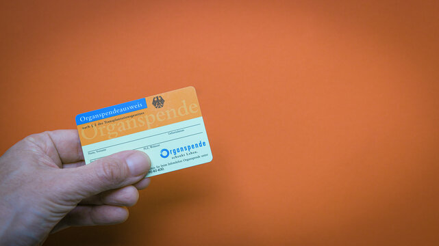 Organspendeausweis vor orangen Hintergrund mit Textfreiraum wird in einer Hand gehalten