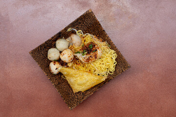 Tom Yum Dry Noodles in Thailand. Noodles with meatballs in a bamboo basket on a brown background.