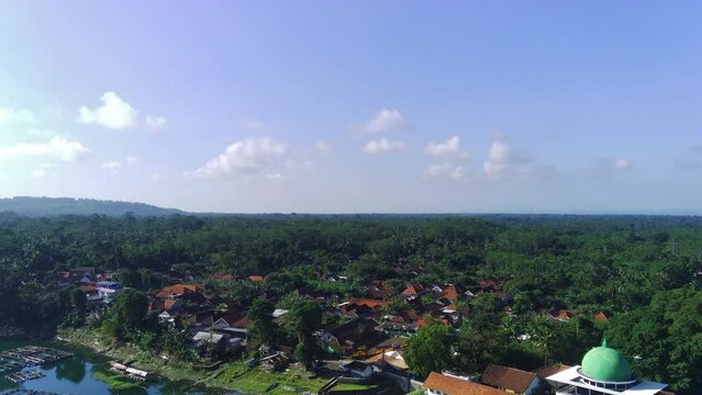A village near Ranu Pakis Lake in Lumajang, East Java, Indonesia on the shore of a blue lake surrounded by trees.