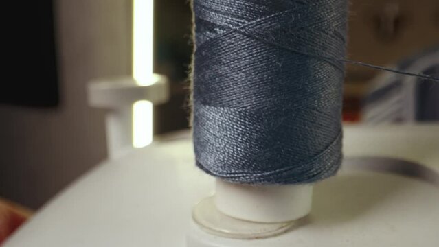 Blue cotton spool thread unwinds on a sewing machine. Spinning roll of threads spins. Close up, selective focus. Needlework and handmade patchwork hobby.
