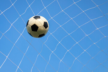 Soccer ball in a goal net under blue sky. Sport exercise of football team concept with copy space.