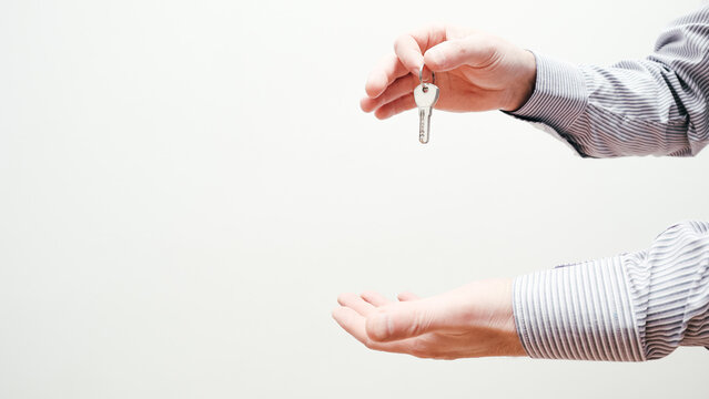 Hand holding house keys. Moving house, relocation. Caucasian male hand holding key to house on white background. Copy space