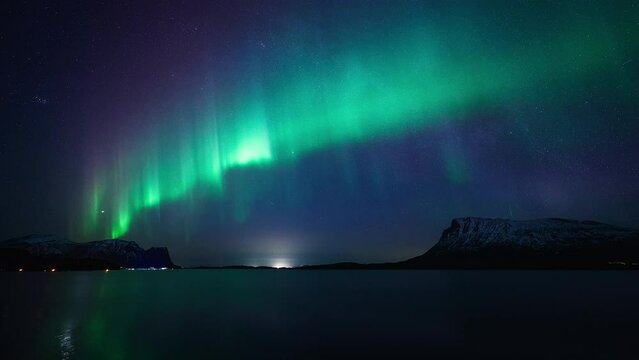 A magnificent dancing aurora and the milky way crossing paths above mountainous fjords of northern Norway.