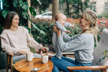Woman friends bonding with baby while sitting in cafe and talking.