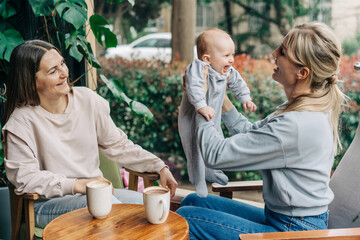Woman friends bonding with baby while sitting in cafe and talking.