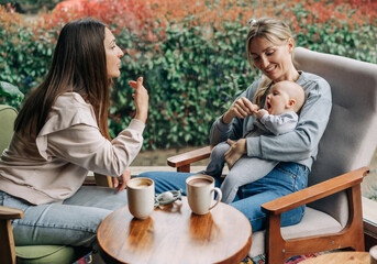 Two friends talk and gossip while sitting in a cafe and taking care of the baby.
