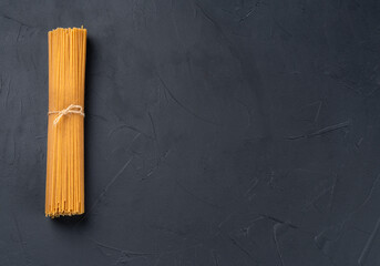 Bunch of raw spaghetti pasta on dark empty background, top view. Copy space