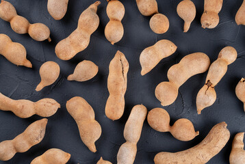Background of scattered tamarind fruits in shell on a dark background, top view