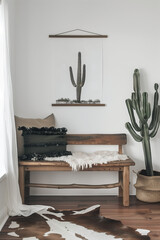 Naklejka premium Minimalist Western style wooden bench with cactus, white wall, black and brown cowhide rug, boho pillows, cacti in the background, hanging canvas art in the style of on simple wood frame.