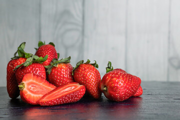 Strawberries with stems on a black table and wooden, light background.