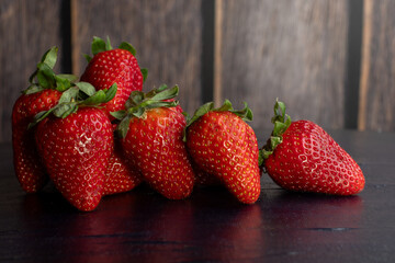 Strawberries with stems on a black table and wooden, brown background.