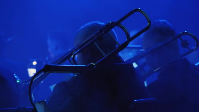 The musicians play trumpet and trombone in a brass band on a dimly lit stage. The blue tones and shadows create an intimate, moody atmosphere, emphasising the artistic character of the scene