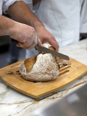 baker cutting bread with a knife on wooden board