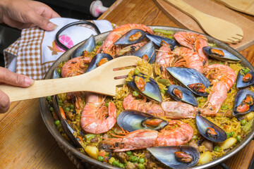 Traditional seafood paella with prawns and mussels in a pan, served with a wooden spoon, typical...