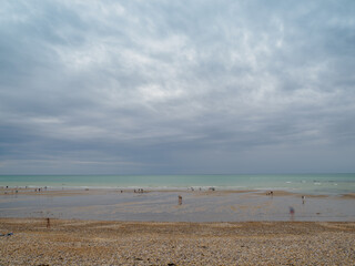 Landscape with dramatic sky. People walking on the shore and bathing in the sea. The sea coast between Audresselles and Ambleteuse. Waters of the English Channel - The La Manche Channel. France.