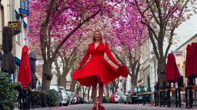 Beautiful blonde girl in red dress on a pink cherry blossom alley in Bonn Germany. High quality 4k footage