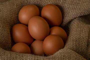 Fresh chicken eggs in a basket on a sack, egg day, wooden table.Selective focus