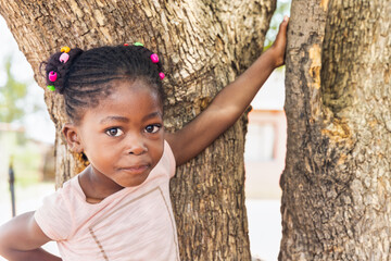 village african girl with braids standing in front of a tree, in the yard