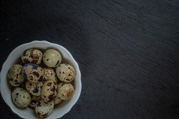 Fresh quail eggs in white plate on black stone, selective focus