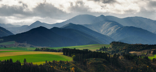 Mountain landscape. In the foreground, a farmland and autumn trees. In the distance you can see the...