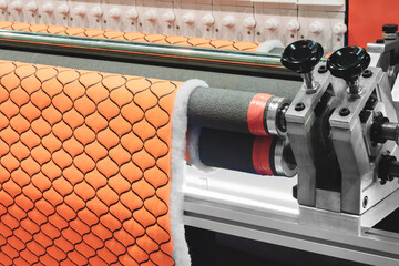 A machine is making a piece of orange fabric with a pattern of squares. The machine is made of...