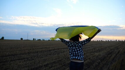 Ukrainian woman running with raised flag Ukraine above her head on wheat field at sunset. Lady jogging with national blue-yellow banner on barley meadow at sunrise. Victory against russian aggression. - 766465807