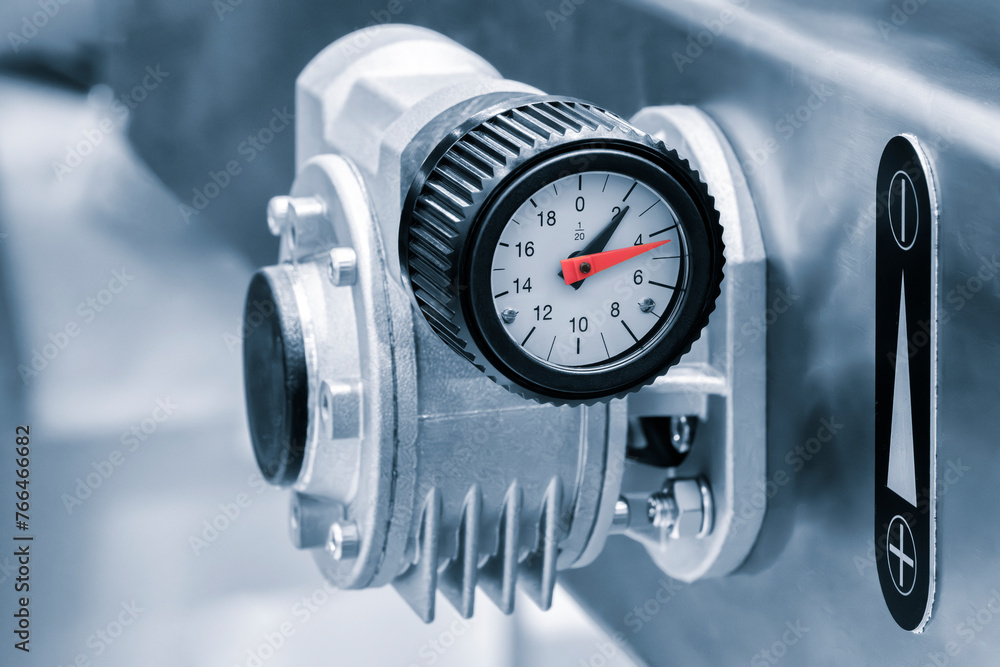 Poster A small black and silver device with a red number 12 on it. The device is attached to a wall. Pressure gauge, thermometer or other measuring instrument on an industrial machine or conveyor