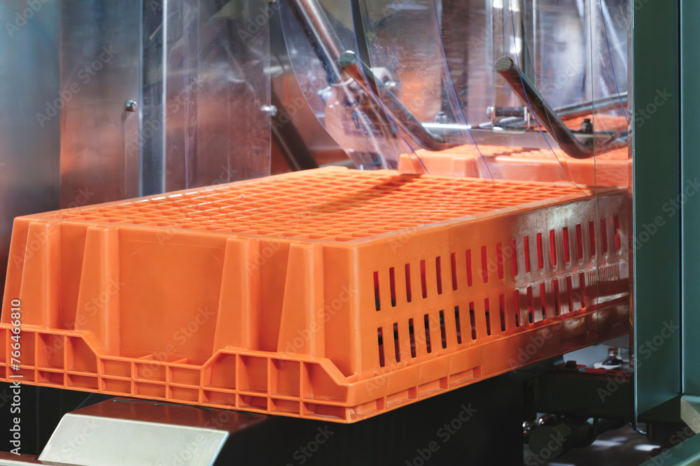 Poster a machine is making a crate out of plastic. the crate is orange and has holes in it, industrial wash