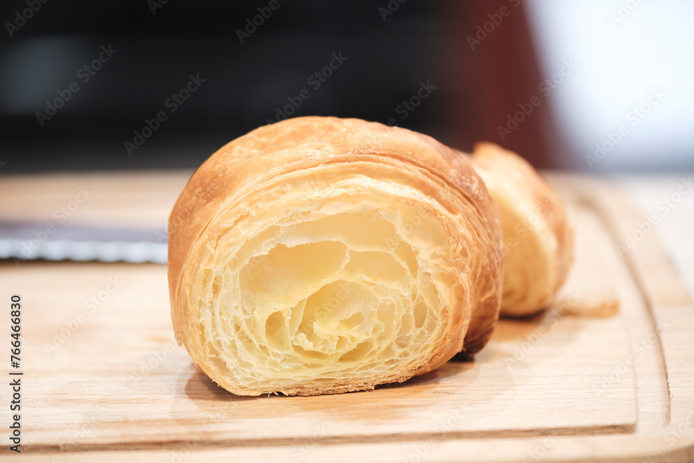 Poster a piece of croissant is cut in half and placed on a wooden cutting board. the croissant is golden br
