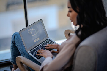 An african american woman sitting an armchair and typing on laptop keyboard