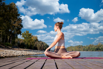 Full length of a woman sitting on the pier by the river and practicing yoga - 766470677