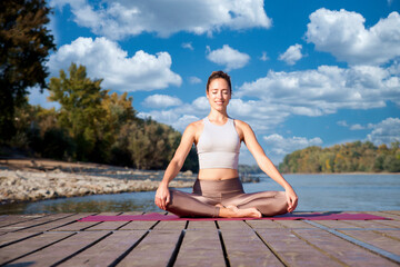 Full length of a woman sitting in lotus pose and practicing yoga outdoor by the Danube river - 766470689