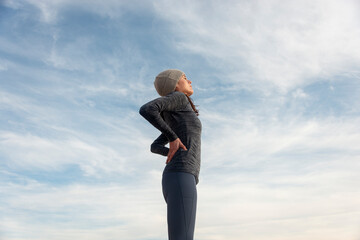 Woman athlete pausing to relieve her back pain holding her hand to her lower back with a grimace...