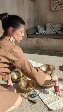 a beautiful woman yogi in an elegant dress moves a stick along a singing Indian bowl