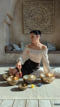 a beautiful woman yogi in an elegant dress moves a stick along a singing Indian bowl