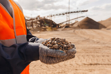 Worker engineer hold gravel in hand, checks quality at sand quarry. Industrial construction site...