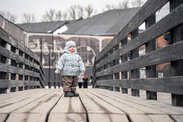 A little girl child toddler on a wooden bridge in the park in the cold season