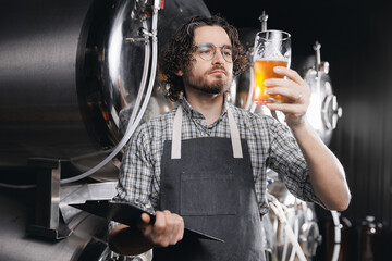 Brewer with clipboard examining control quality and color of drink production. Worker sommeliers...