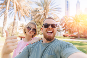 Selfie photo of happy couple young man and woman tourists background park with palm and skyscrapers...