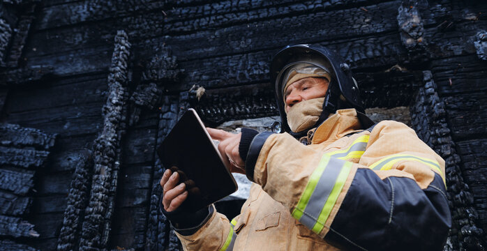 Fireman inspector officer inspects burnt house, take photo on tablet for report of investigating incident fire. Control safety after burning apartment