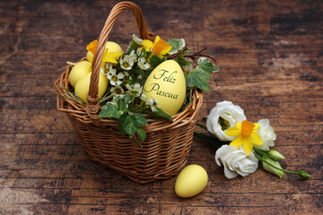 Cesta decorativa de Pascua con narcisos, hiedra y un huevo de Pascua con el texto Felices Pascuas.