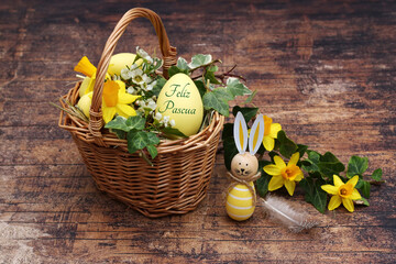Cesta decorativa de Pascua con narcisos, hiedra y un huevo de Pascua con el texto Felices Pascuas. - obrazy, fototapety, plakaty