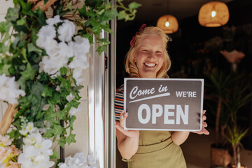 Florist holding an 'open' sign at her shop - obrazy, fototapety, plakaty