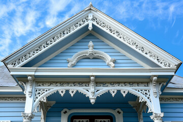 A close-up of the ornamental pediments and cornices of an Italianate porch, showcasing the house against a sky blue backdrop - Powered by Adobe